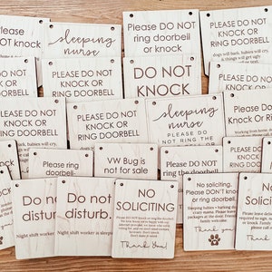 May include: A collection of rectangular wooden signs with various phrases in black lettering. Common phrases include "Please Do Not Knock" and "No Soliciting." Some signs feature a paw print.