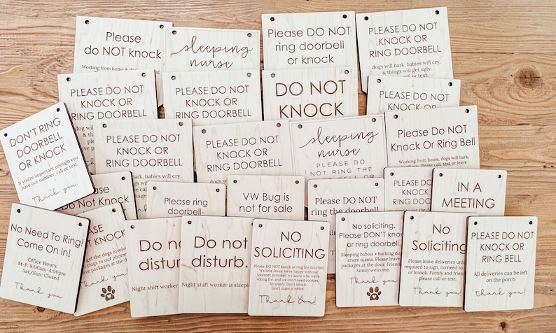 May include: A collection of rectangular wooden signs with various phrases in black lettering. Common phrases include "Please Do Not Knock" and "No Soliciting." Some signs feature a paw print.