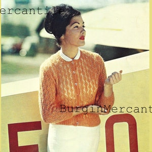 May include: A woman wearing a peach-colored knitted cardigan with a white collar and a white skirt. The cardigan has a delicate lace pattern. The text "Burgin Mercantile" is visible in the image.