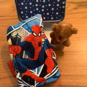 May include: A blue and red fabric pouch with a Spiderman image, a brown teddy bear, and a blue tin with white stars.