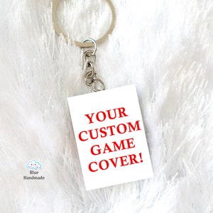 May include: White keychain with a silver key ring and a white square tag with the red text "YOUR CUSTOM GAME COVER!"