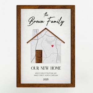 May include: A framed print with a brown wooden frame. The print features a house-shaped design with a map inside, a red heart, and the text "The Brown Family" and "OUR NEW HOME". The address and year 2025 are also included.