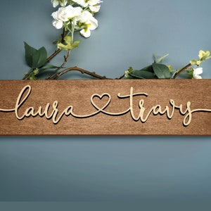 May include: A wooden sign with the names "Laura" and "Travis" written in cursive script with a heart symbol between the names.