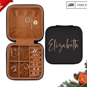 May include: Black faux leather jewelry box with a brown velvet interior. The box has a hinged lid and a removable tray with compartments for earrings, rings, and other jewelry. The lid has the name "Elizabeth" written in gold lettering.