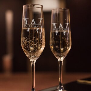 May include: Two clear champagne flutes filled with sparkling wine. The flutes are engraved with the text "Williams" and a stylised "W".