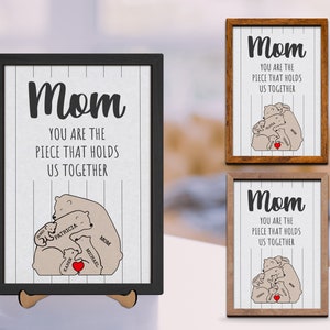 May include: A framed print with a white background and black stripes. The print features a drawing of a mother bear and her cubs with the text "Mom You Are The Piece That Holds Us Together". The cubs are labeled with names.