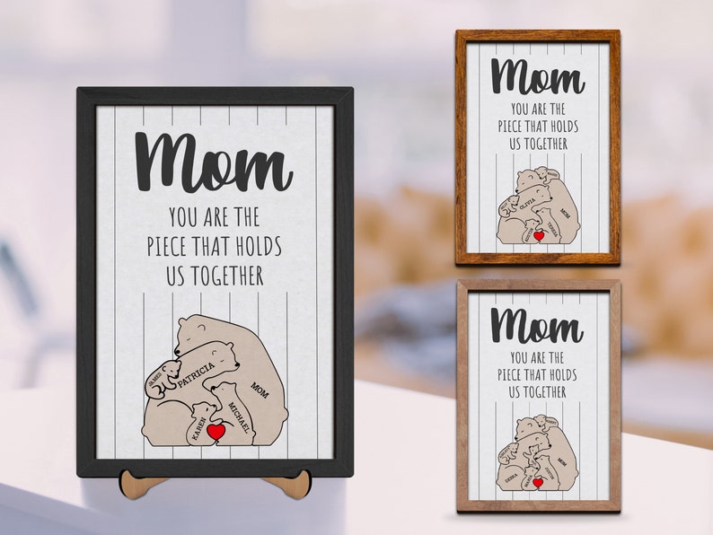May include: A framed print with a white background and black stripes. The print features a drawing of a mother bear and her cubs with the text "Mom You Are The Piece That Holds Us Together". The cubs are labeled with names.