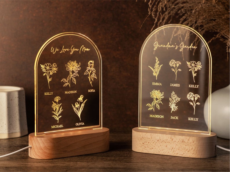May include: Two illuminated acrylic plaques with wooden bases. One reads "We Love You Mom" with floral illustrations and names. The other says "Grandma's Garden" with flowers and names. Both have a warm glow.