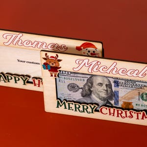 May include: Two wooden picture frames with Christmas themes. The top frame says "Thomas" and "Happy Holidays". The bottom frame says "Micheal" and "Merry Christmas".