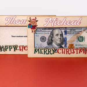 May include: Two wooden picture frames with a Christmas theme. The frame on the left says "Thom Happy Holidays" and the frame on the right says "Micheal Merry Christmas". Both frames have a dollar bill inside.