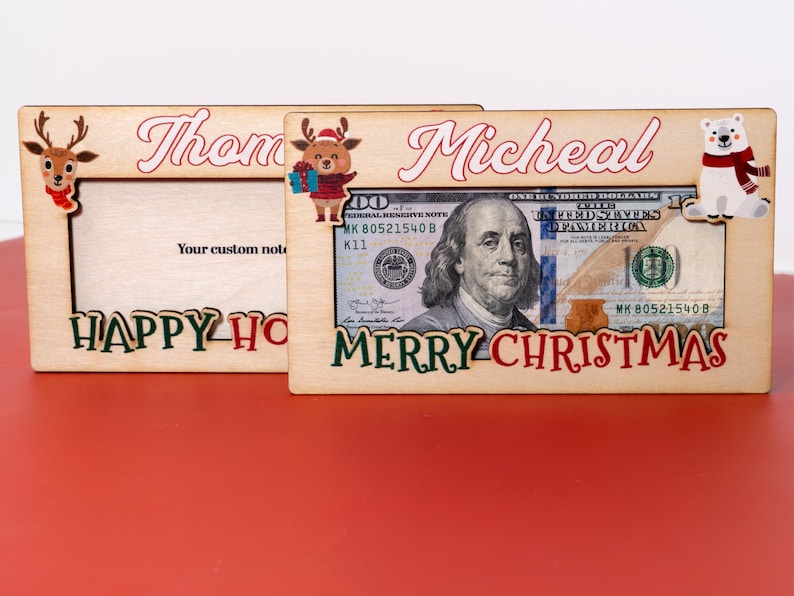 May include: Two wooden picture frames with a Christmas theme. The frame on the left says "Thom Happy Holidays" and the frame on the right says "Micheal Merry Christmas". Both frames have a dollar bill inside.