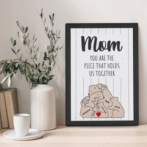 May include: A black framed print with a white background and black stripes. The print features a graphic of a family of bears with the text "Mom You are the piece that holds us together". The bears are labeled with names like "Mom", "William", "Mary", and "Jennifer".