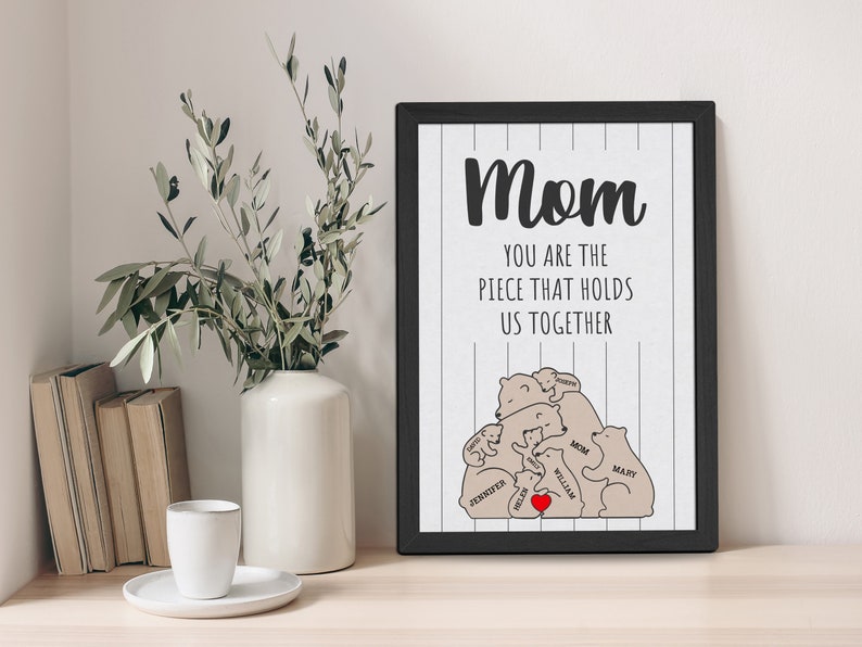 May include: A black framed print with a white background and black stripes. The print features a graphic of a family of bears with the text "Mom You are the piece that holds us together". The bears are labeled with names like "Mom", "William", "Mary", and "Jennifer".