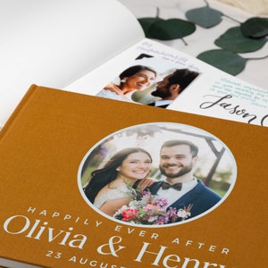 May include: A brown photo album with a circular cutout on the front cover. The cutout shows a photo of a couple smiling at the camera. The text "Happily Ever After Olivia & Henry 23 August" is printed on the front cover.