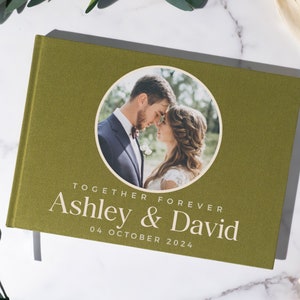 May include: A green linen wedding guest book with a circular photo of a couple on the front. The text "Together Forever Ashley & David 04 October 2024" is printed on the front.