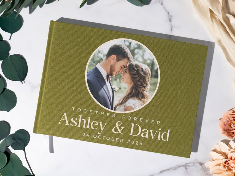 May include: A green linen wedding guest book with a circular photo of a couple on the front. The text "Together Forever Ashley & David 04 October 2024" is printed on the front.