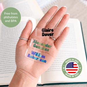 May include: Three rectangular clear acrylic name tags featuring custom printed names. The top tag displays Claire Dover in black, the middle tag shows Alexander Gonzales in green, and the bottom tag features William Robertson in blue text.