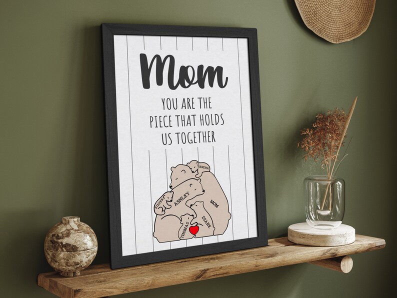 May include: A black framed print with the text "Mom you are the piece that holds us together" and a graphic of a family of bears hugging each other. The bears are labeled with names like "Mom", "Ashley", "Thomas", "Ethan", and "Sarah".