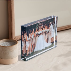 K&ouml;nnte beinhalten: Ein klarer Acrylblock-Bilderrahmen mit einem gedruckten Bild einer Gruppe von Personen auf einer Hochzeit. Die Braut tr&auml;gt ein wei&szlig;es Kleid und die Brautjungfern tragen pfirsichfarbene Kleider.