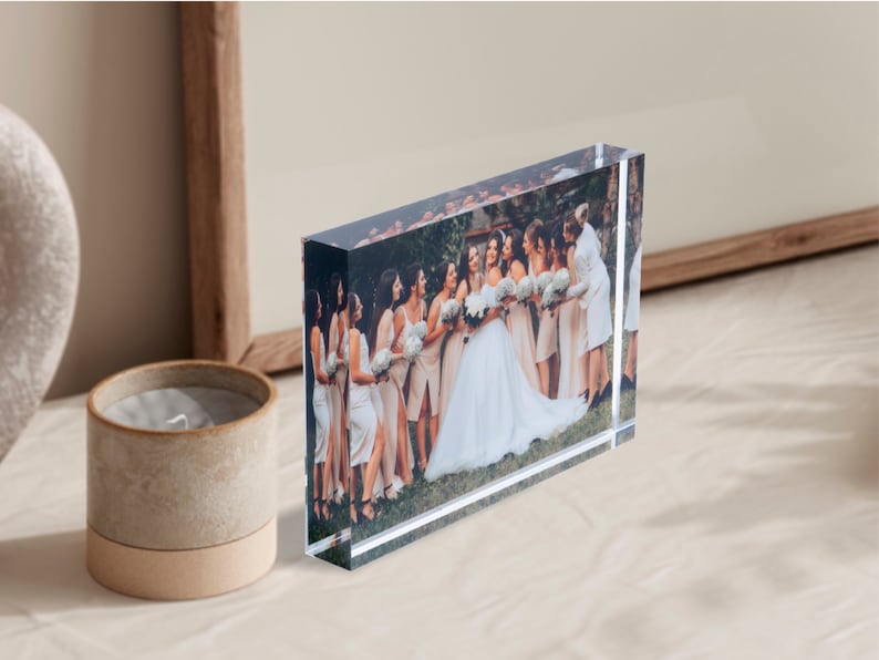 K&ouml;nnte beinhalten: Ein klarer Acrylblock-Bilderrahmen mit einem gedruckten Bild einer Gruppe von Personen auf einer Hochzeit. Die Braut tr&auml;gt ein wei&szlig;es Kleid und die Brautjungfern tragen pfirsichfarbene Kleider.