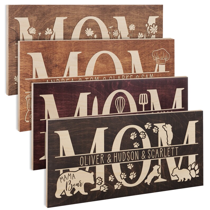 May include: Five wooden signs with the word "MOM" in large, white letters. Each sign has a different design and personalization. The top sign has small flowers, the second sign has a chef's hat and the names "Andrea, Tom, Clarke & Sam", the third sign has a whisk and spatula, the fourth sign has paw prints and the names "Oliver & Hudson & Scarlett", and the bottom sign has a bear and the words "Mama Bear".