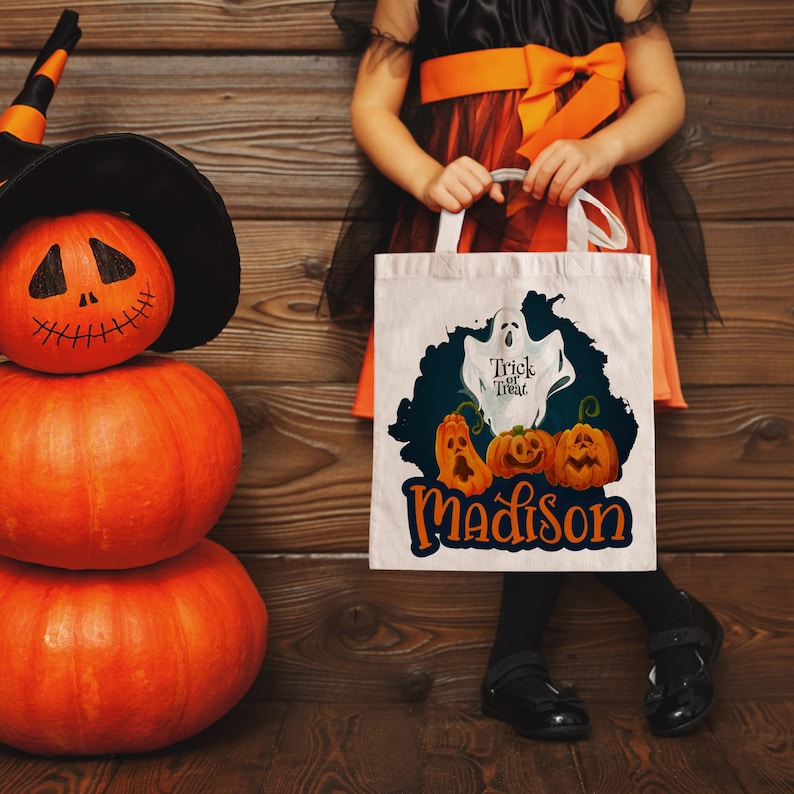 May include: A white canvas tote bag with a ghost and pumpkins design. The bag has the text "Trick or Treat" and the name "Madison" printed on it.