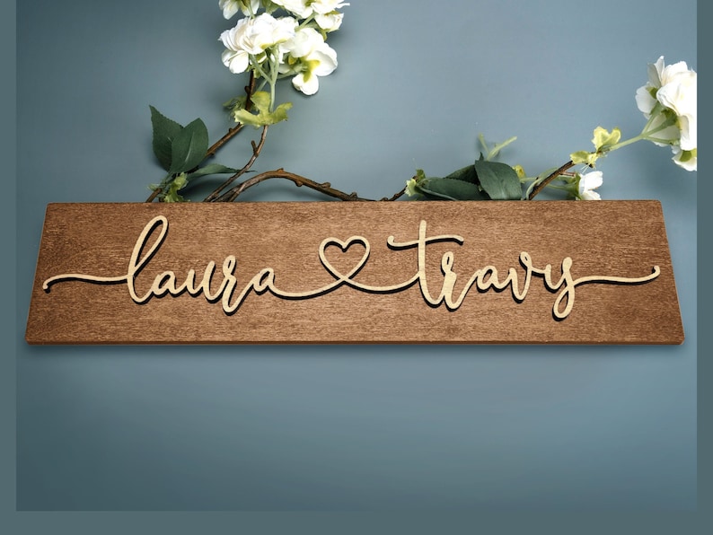 May include: A wooden sign with the names "Laura" and "Travis" written in cursive script with a heart symbol between the names.