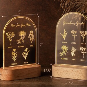 May include: Two illuminated acrylic signs with wooden bases. One reads "We Love You Mom" with floral designs and names. The other says "Grandma's Garden" with floral designs and names. Each sign is 7 inches tall and 5 inches wide.