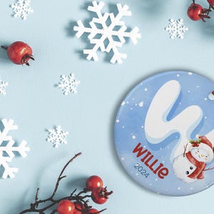 May include: A blue and white Christmas ornament with a snowman and the name "Willie" and the year "2024" written on it.