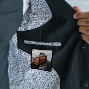 May include: A dark blue suit jacket with a white and black patterned lining. A small photo of a couple is visible in the pocket.