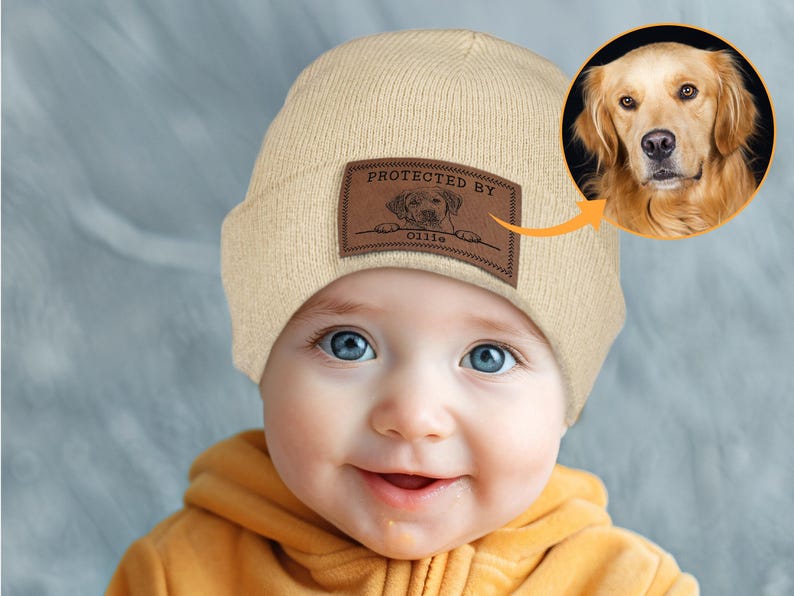 May include: A beige knitted beanie with a brown leather patch that says "Protected by Ollie" and a picture of a golden retriever dog.