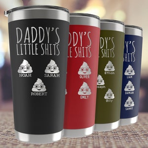 Op de afbeelding: Vier roestvrijstalen bekers met een humoristisch ontwerp. Elke beker heeft een cartoon-poep-emoji met een bril en een naam eronder. De tekst op de bekers luidt "Daddy's Little Shits".