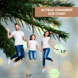 May include: A family of three, a man, a woman, and a child, are jumping in the air. They are all smiling and holding hands. The image is a 3.5 inch by 3.5 inch acrylic ornament.  Acrylic Ornament Size Chart.