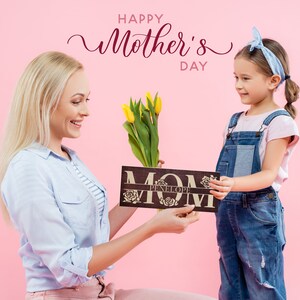May include: A young girl gives her mother a wooden sign that says "MOM" with the name "PENELOPE" engraved on it. The sign is decorated with roses. The girl is holding a bouquet of yellow tulips. The background is pink and the text "HAPPY MOTHER'S DAY" is written in pink.