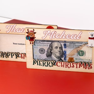 May include: Two wooden picture frames with a Christmas theme. The top frame says "Thon" and the bottom frame says "Micheal" with a dollar bill and a polar bear illustration. Both frames say "Happy Holidays" and "Merry Christmas".
