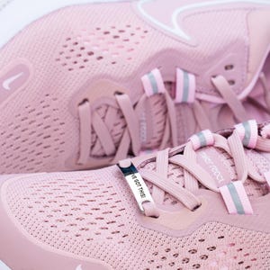 Puede incluir: Un par de zapatillas de running rosas con un logotipo Swoosh blanco y un charm plateado que dice "I've got this". Las zapatillas tienen una parte superior de malla y una suela blanca.