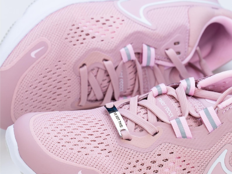Puede incluir: Un par de zapatillas de running rosas con un logotipo Swoosh blanco y un charm plateado que dice "I've got this". Las zapatillas tienen una parte superior de malla y una suela blanca.