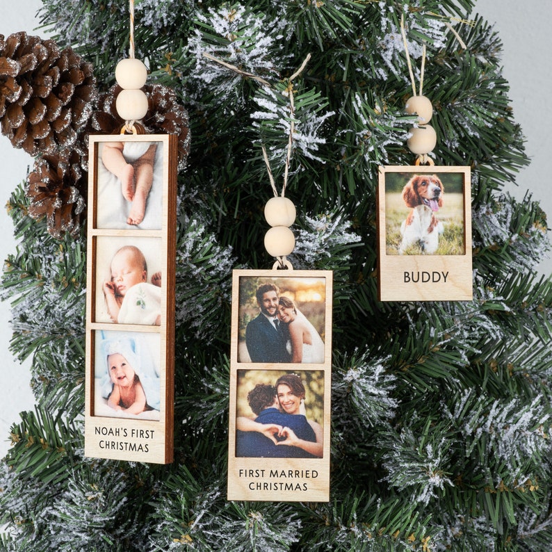 May include: Three wooden photo ornaments with twine hangers and wooden beads. The ornaments feature photos of a baby, a couple, and a dog. The ornaments have text that reads "Noah's First Christmas", "First Married Christmas", and "Buddy".