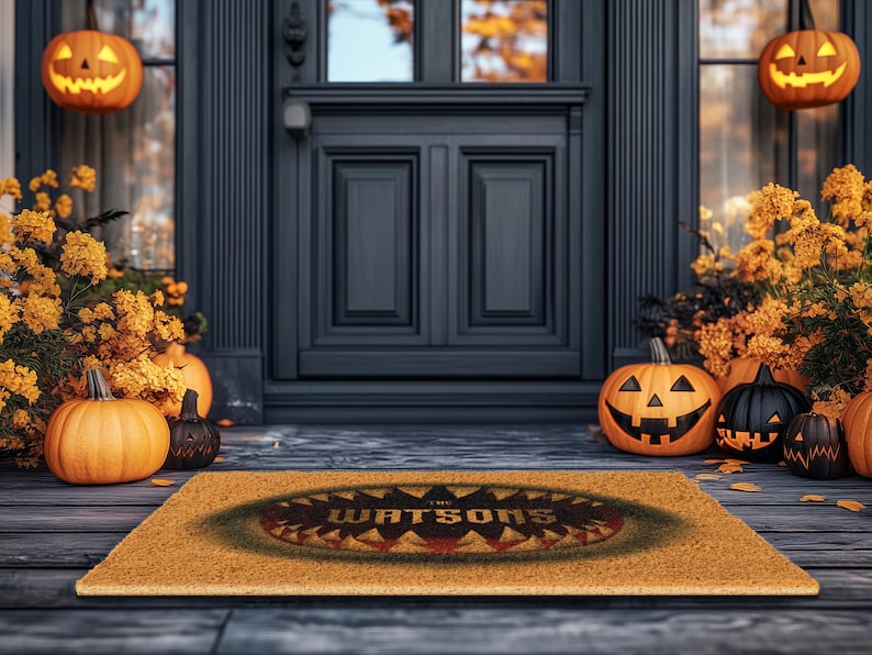 Pu&ograve; includere: Un tappetino per porta in fibra di cocco marrone con il testo "The Watsons" in un carattere spettrale. Il tappetino &egrave; decorato con un design a tema Halloween nero e arancione. Il tappetino &egrave; posizionato su un portico in legno con zucche e foglie autunnali.