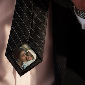 May include: A black and white striped tie with a small photo of a woman and a baby on the front. The photo is in a clear plastic frame.