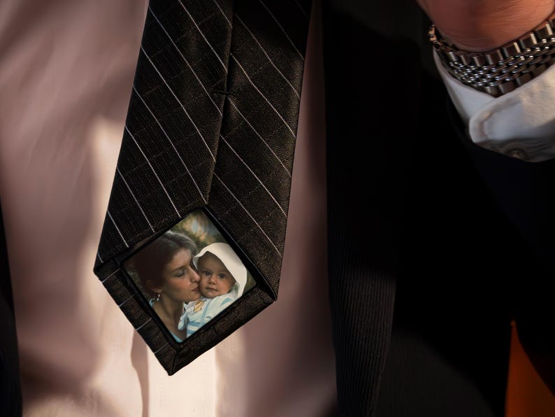 May include: A black and white striped tie with a small photo of a woman and a baby on the front. The photo is in a clear plastic frame.