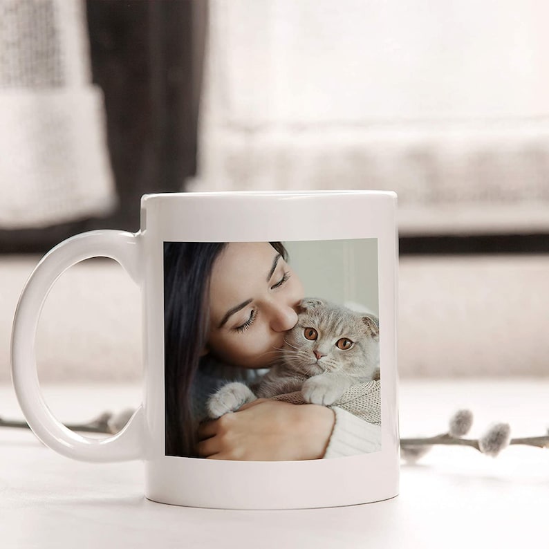 May include: White ceramic mug with a photo of a woman kissing a cat on the front.