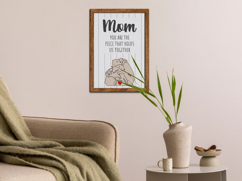 May include: A framed print with a white background and wood-grain frame. The print features a drawing of three bears hugging with a heart in the center. The text reads "Mom you are the piece that holds us together".