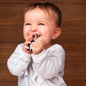 Pu&ograve; includere: Un bambino che indossa un body a righe bianche e grigie sta ridendo mentre tiene in mano un giocattolo di pinguino bianco e nero. Il giocattolo ha una piccola faccia.
