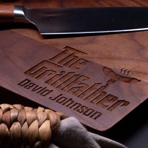 May include: A personalized walnut cutting board with the text "The Grillfather David Johnson" and a stylized image of a hot dog and fork.