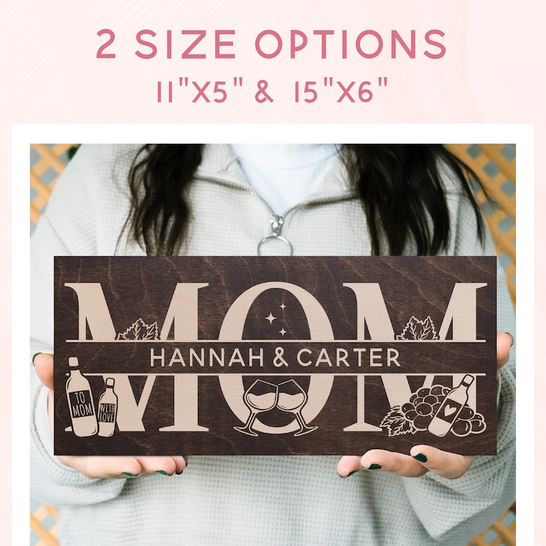 May include: A brown wooden sign with the word "MOM" in large, white letters. The sign also includes the names "HANNAH & CARTER" and images of wine bottles, glasses, and grapes.