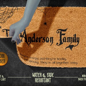 Pu&ograve; includere: Un tappetino per porta in fibra di cocco marrone con un design a ragnatela nero e il testo "Anderson Family" in un carattere gotico nero. Il testo sottostante recita "They're creepy and they're kooky, and spooky. They're all together ooky."