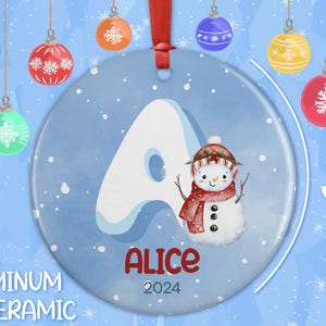 May include: A blue and white Christmas ornament with a snowman and the letter A. The ornament is 3 inches in diameter and says "Alice 2024".