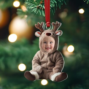 Pu&ograve; includere: Un ornamento natalizio con un bambino vestito con un costume da renna marrone. L'ornamento &egrave; in metallo e ha un nastro rosso attaccato alla parte superiore.