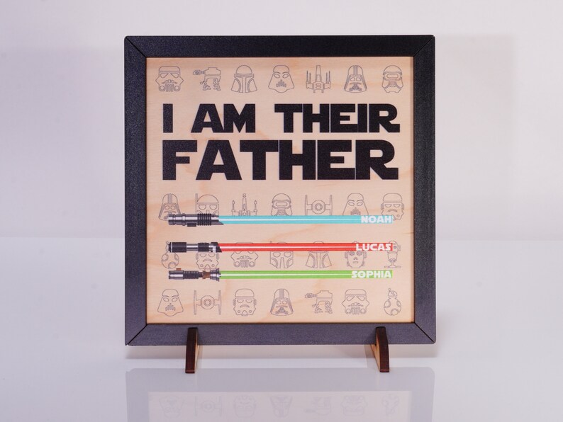 May include: Wooden framed sign with the text "I AM THEIR FATHER" in black. Below are three lightsabers in blue, red, and green, each with a name. The background features Star Wars character illustrations.